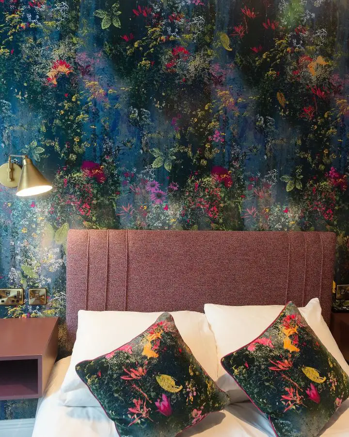 Dark floral wallpaper bedroom from @mairihelena. Navy background with vibrant botanical prints and coral headboard.
