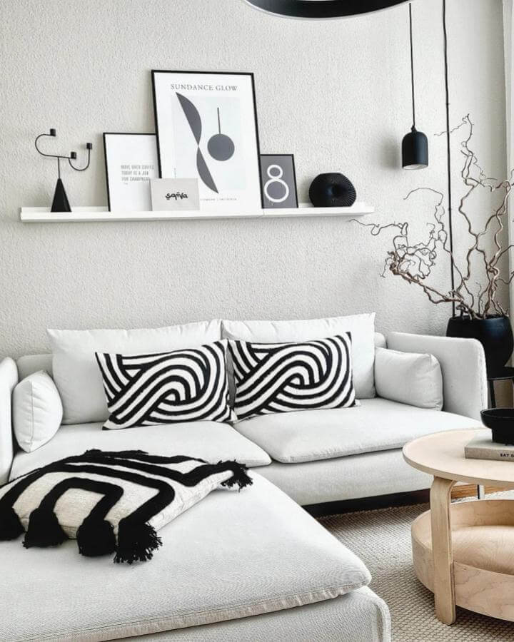White sofa with black and white graphic pillows and matching throw in a modern monochrome living room by @hygge__quartier7 with abstract art and natural wood table.