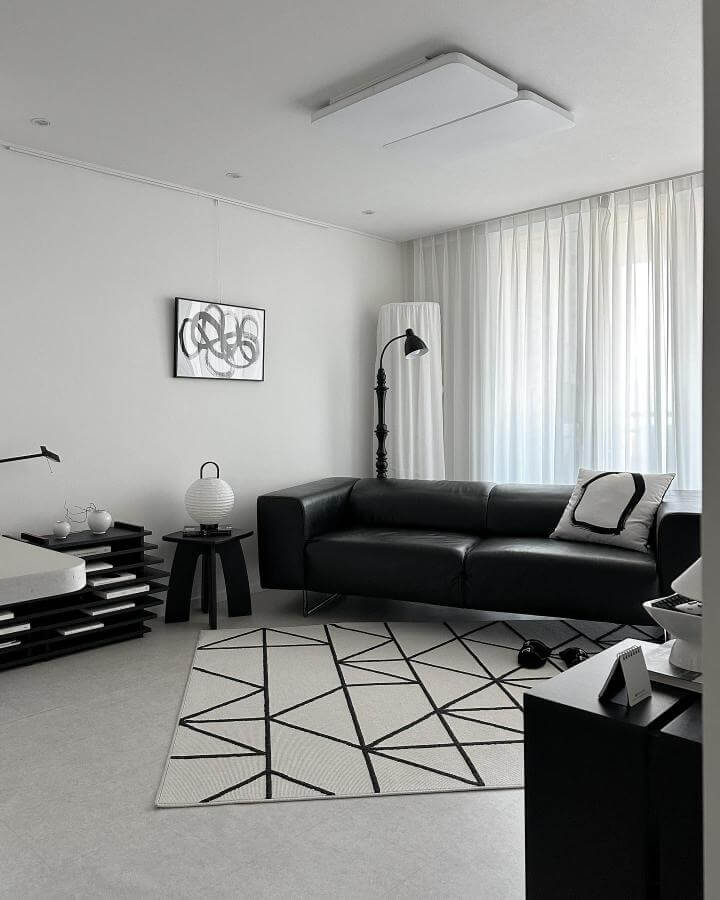 Black and white living room ideas featuring a geometric patterned rug, black leather sofa, sheer curtains, and minimalist decor by @jennyhomemood