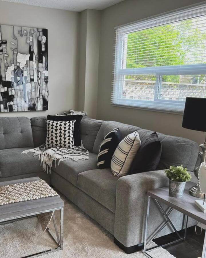 Gray sectional sofa with black and white geometric pillows and abstract wall art in a monochrome living room by @creativedesignshomestaging. Modern cozy style.