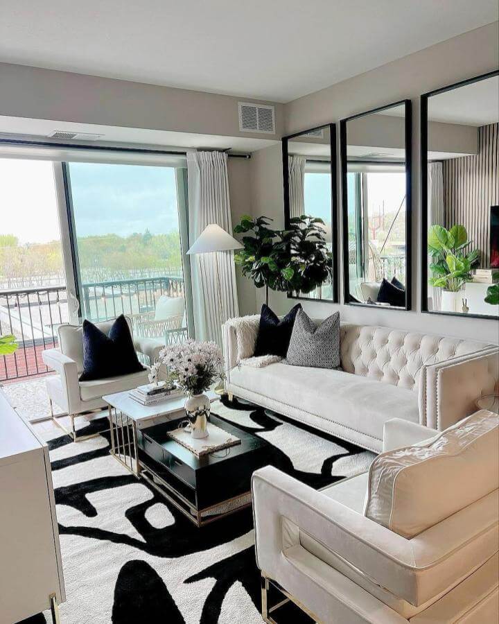 Black and white living room with bold patterned rug, cream velvet sofa and chairs, black framed mirrors by @chic_designs_by_ruthie.