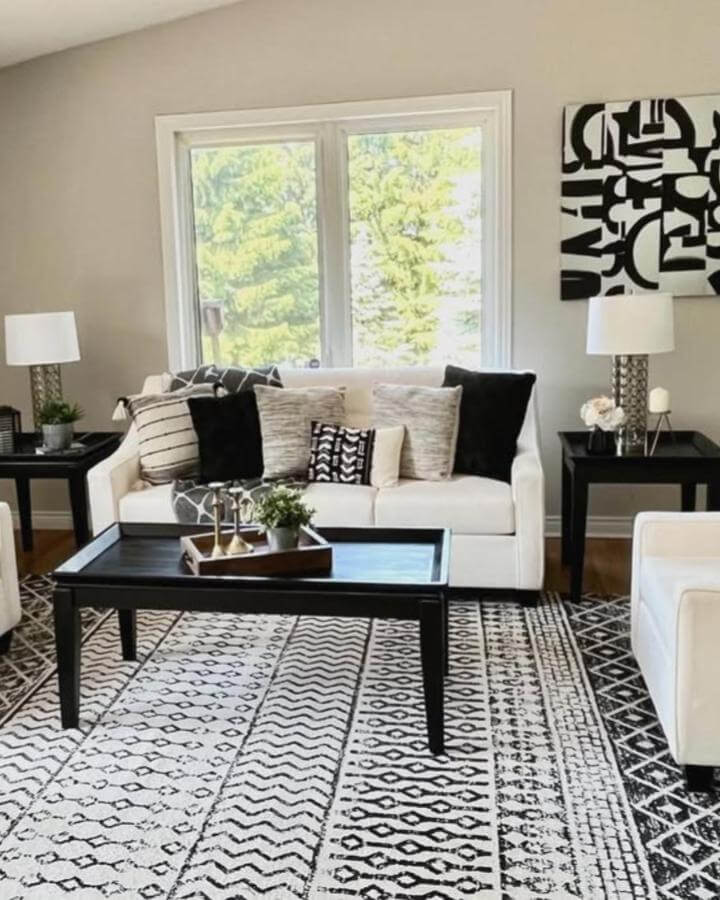 Black and white geometric and tribal patterned rug with white couch, black coffee table, and monochrome throw pillows in a modern living room styled by @creativedesignshomestaging.