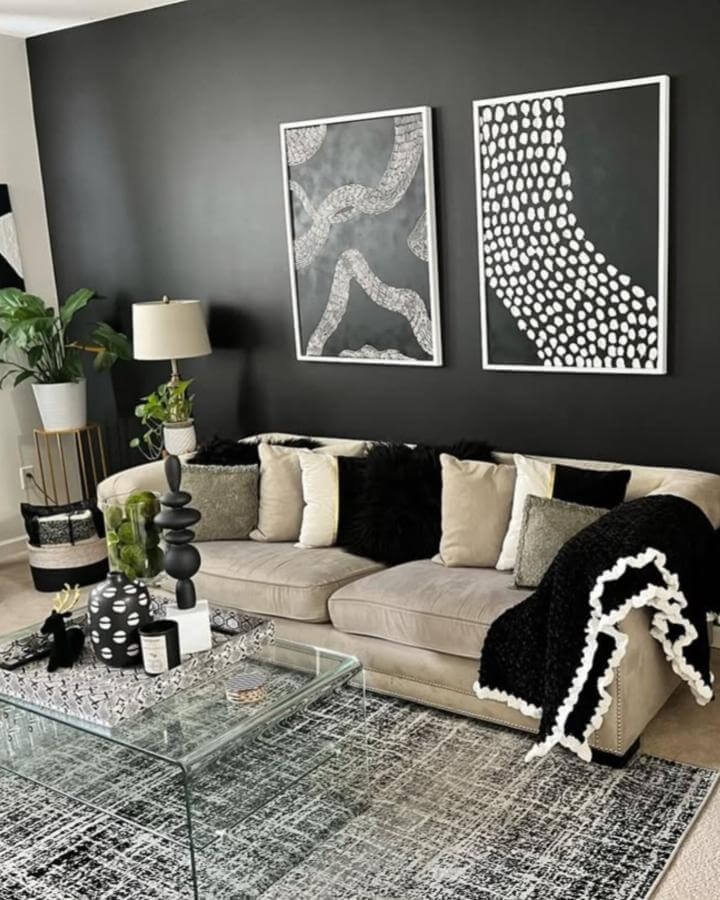 Black matte accent wall with neutral beige sofa and black and white living room ideas from @abrightappeal_homeedition featuring modern abstract art and glass coffee table.