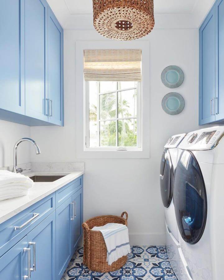 Blue shaker cabinets and patterned tile flooring in cozy laundry room from @brantleyphoto with natural light and woven basket accents.