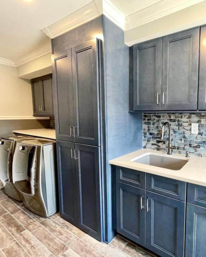 Deep blue cabinetry in laundry with ceramic mosaic backsplash and stainless steel machines from @notjustkitchens_nj. Rich, modern utility space.