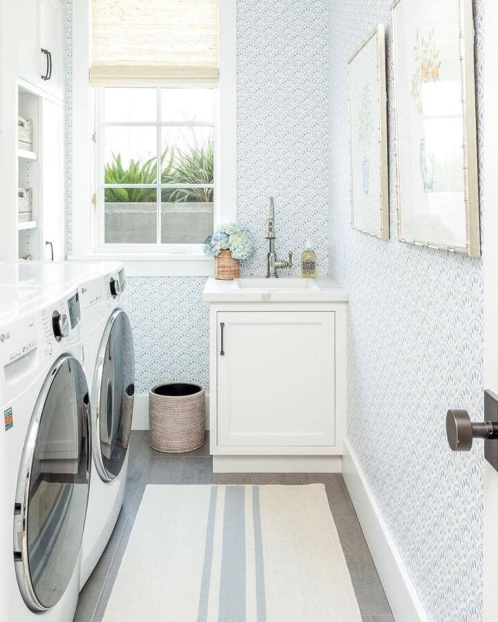 Soft blue patterned wallpaper laundry room with white cabinets and natural accents from @mollyrose.photo Bright and inviting small space design