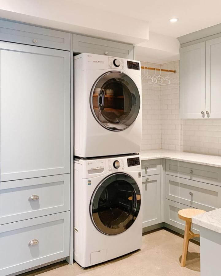 Light soft blue shaker cabinets laundry room with white tile backsplash and wooden stool from @akbdesign. Clean and calming design.