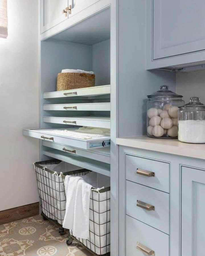 Light blue custom cabinetry laundry space from @marieflaniganinteriors featuring sliding shelves and wire hamper baskets.