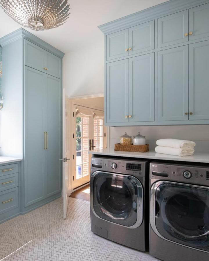 Soft blue painted cabinetry laundry room from @kaceygilpin with brass hardware and white tile flooring.