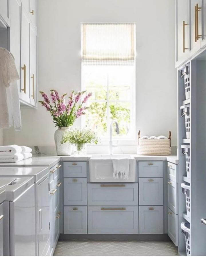 Soft powder blue cabinetry laundry room by @marieflaniganinteriors with brass hardware and natural light near farmhouse sink.