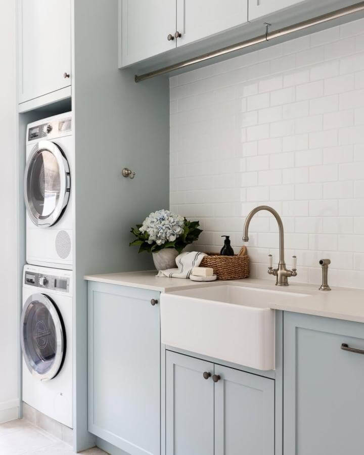 Soft muted blue cabinets and white subway tile laundry room from @simonwhitbreadphoto showing stylish blue laundry room ideas with farmhouse sink.