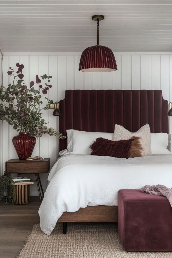 A stylish bedroom featuring burgundy walls, white furnishings, and decor.