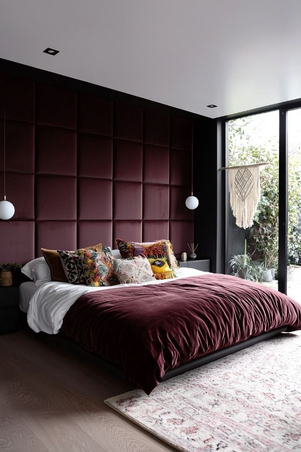 Cozy bedroom featuring a burgundy headboard, eclectic decor, and plants.