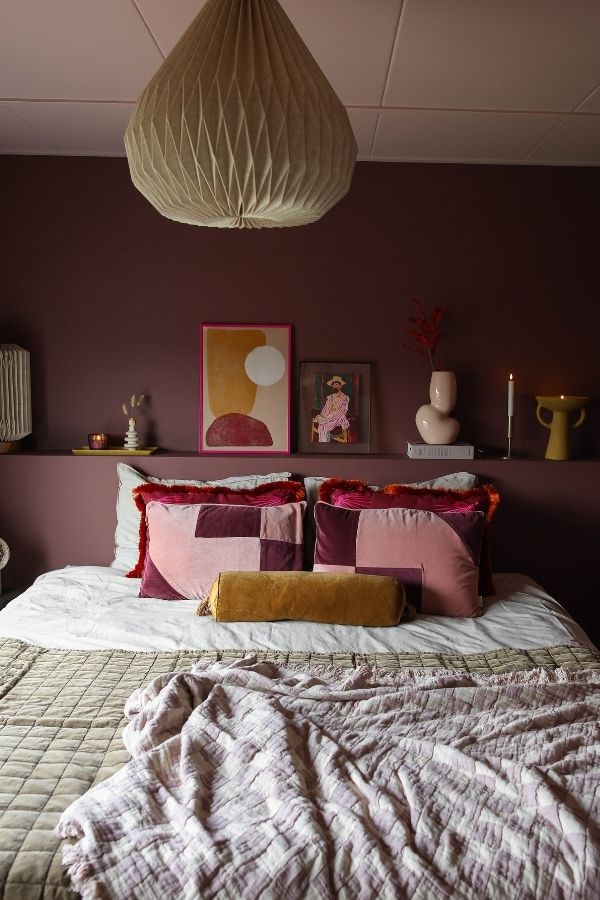 Burgundy and pink cozy bedroom with plush bedding and cushions.