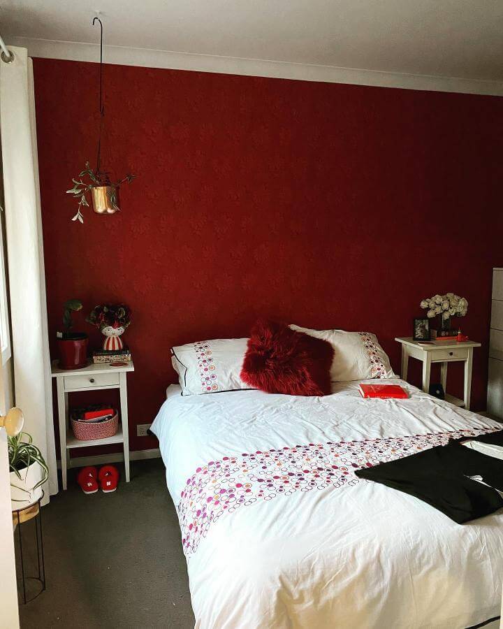 Cherry red textured wall with white and patterned bedding in a cozy bedroom by @_katypop_ featuring layered soft and bold accents.