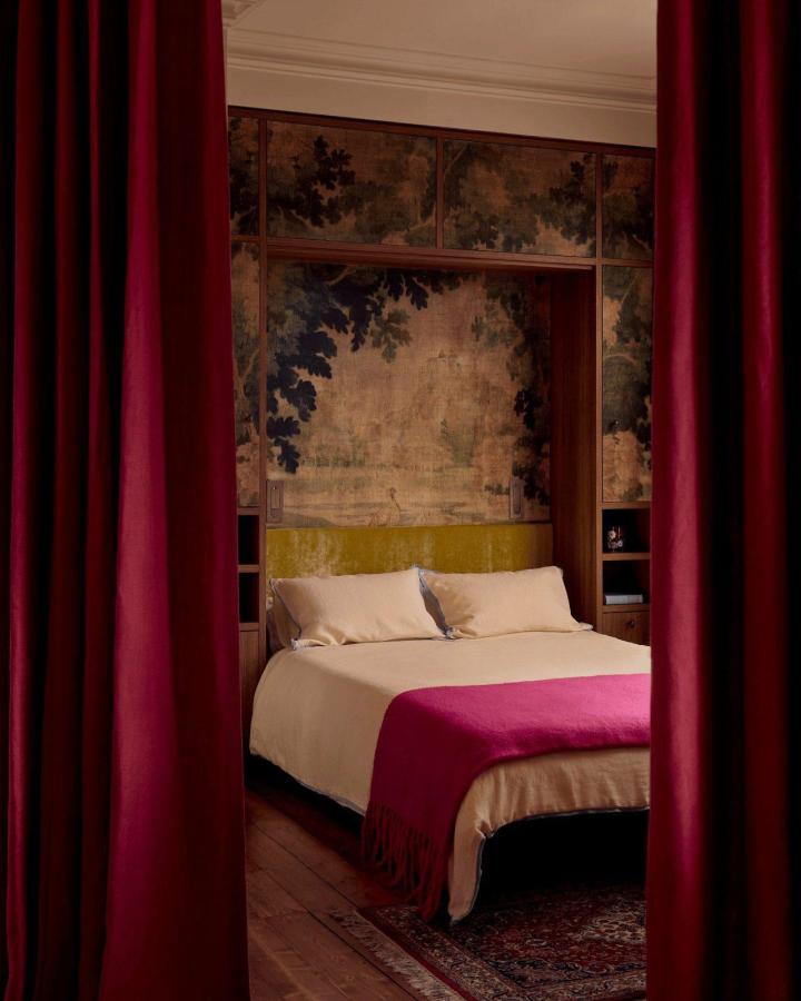 Velvet cherry red curtains framing a cozy bedroom space with cream bedding and vintage mural by @lillie_thompson creating a warm atmosphere