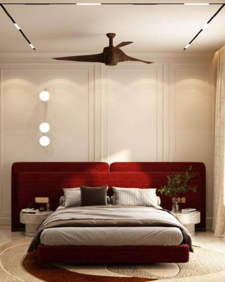 Rich cherry red velvet upholstered bed with cozy pillows and natural textured accents by @tanishabansalinteriors in a warm bedroom setting.