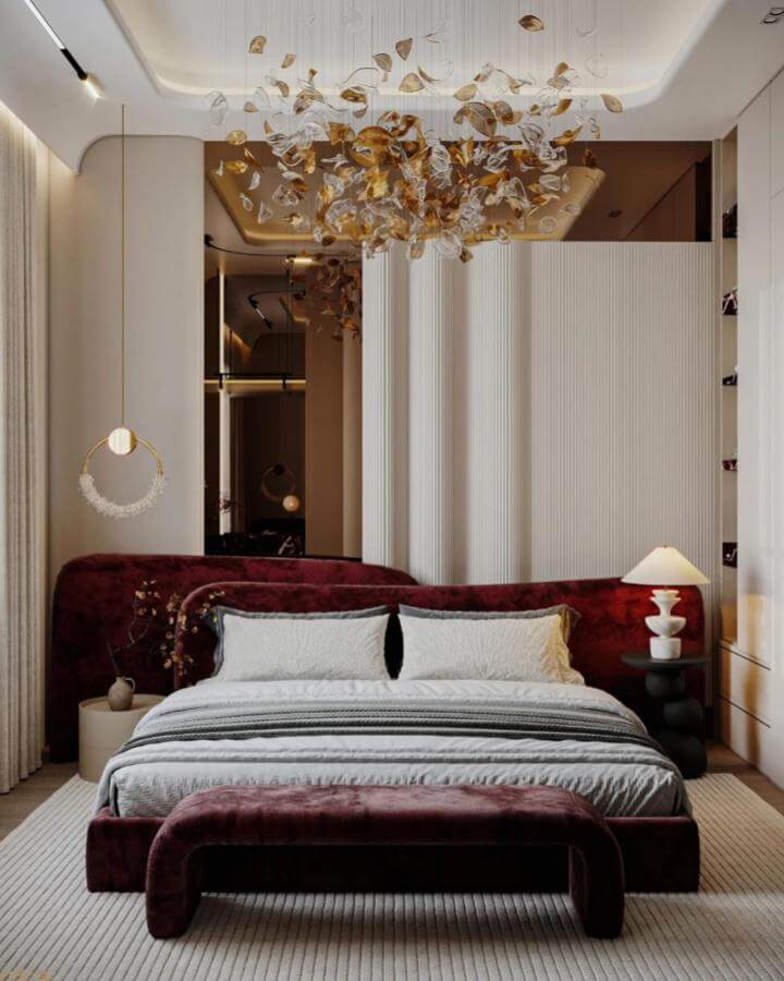 Cherry red velvet bed and bench in a modern bedroom creating bold cherry red bedroom ideas with soft neutral walls and gold glass ceiling art.