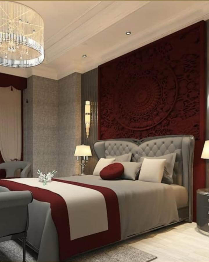 Cherry red carved wall panel and bed linens with gray upholstered headboard from @boracainteriors. Elegant cozy bedroom design.