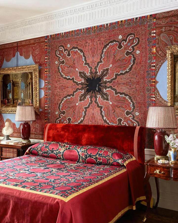 Velvet cherry red bed with Persian tapestry backdrop vintage lamps and gold frames in classic bedroom by @obertogili. Deep reds with intricate patterns create a cozy, ornate vibe.