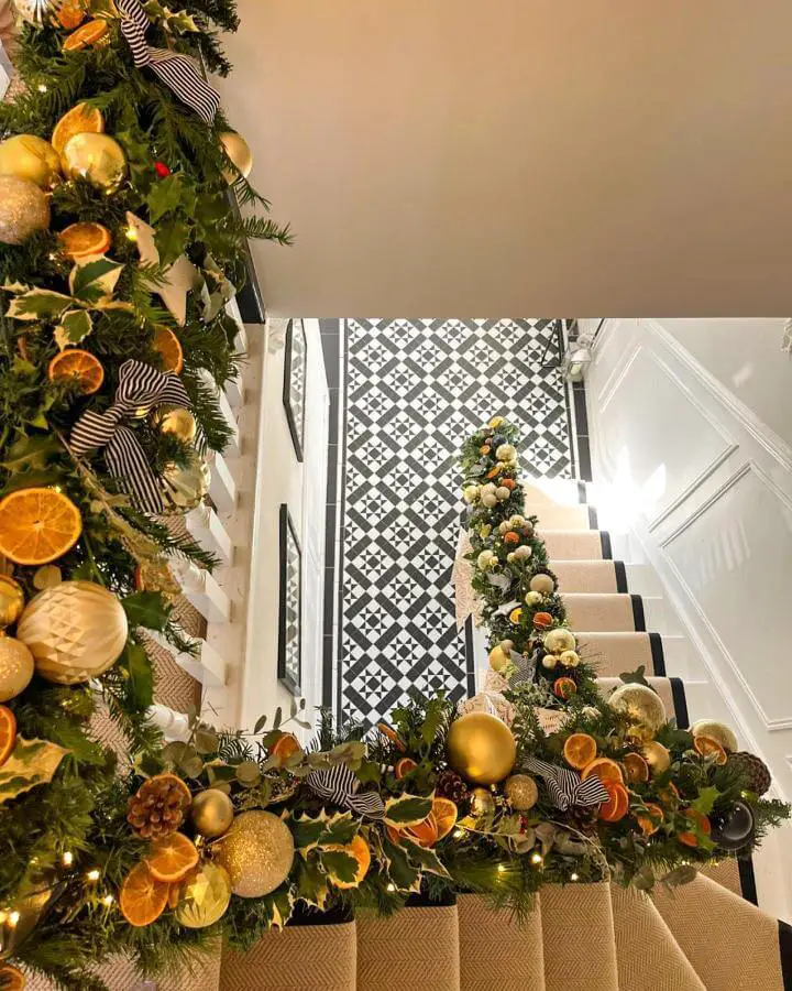 Lush garland with dried oranges and gold ornaments from @se9_edwardian adorning a staircase banister with monochrome tiled floor