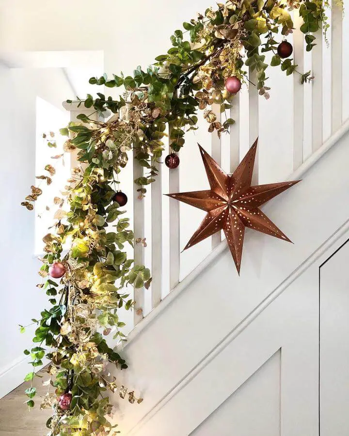 Eucalyptus garland with copper star and ornaments from @firstsenseinteriors draped on white staircase railing.