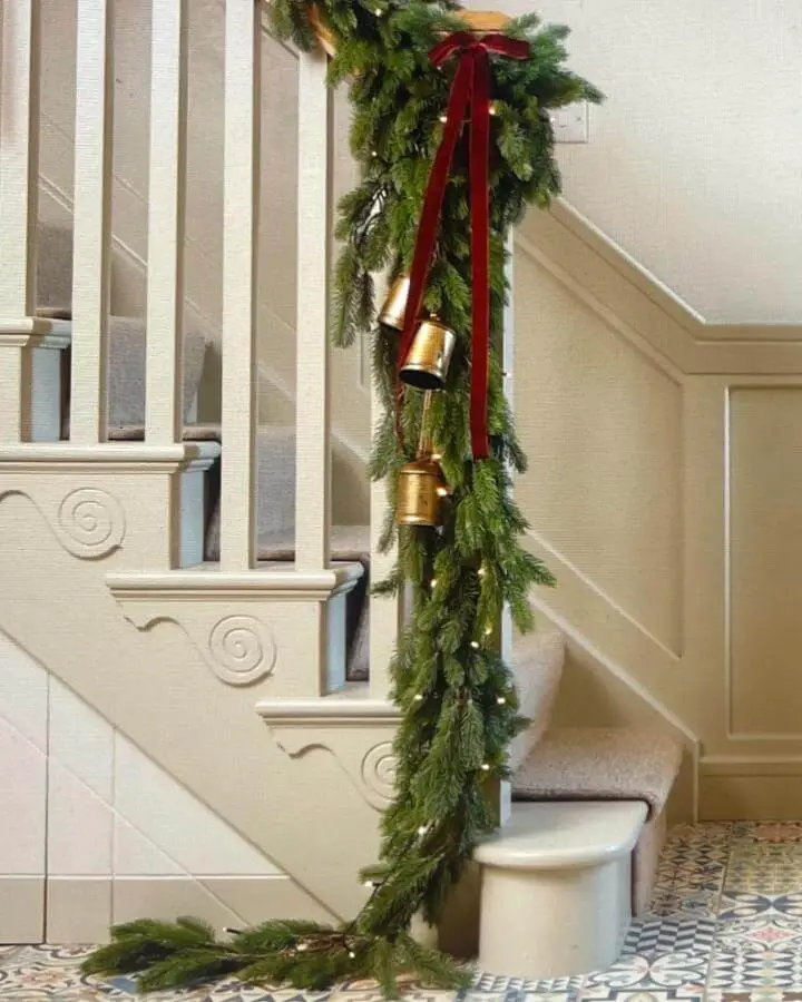 Fresh evergreen garland with brass bells and burgundy ribbon from @mrsgoughshomedecor. Elegant holiday staircase styling.