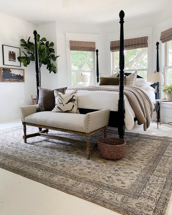 Black four-poster bed from @rignellranch featuring cream bench and bamboo blinds in neutral bedroom setting.