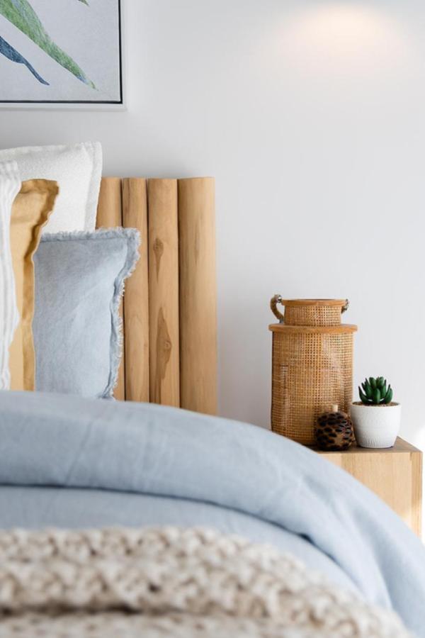 Natural wood slat headboard from @hotondohomes. Soft blue bedding and woven rattan basket complete the look.