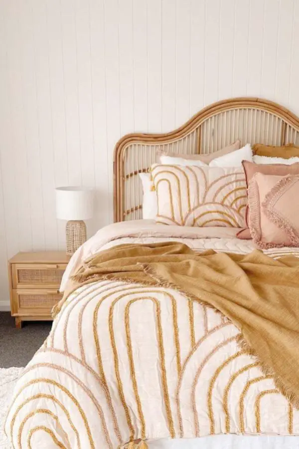 Curved rattan headboard from @koko.collective. Features tufted rainbow bedding with peachy pink accent pillows.