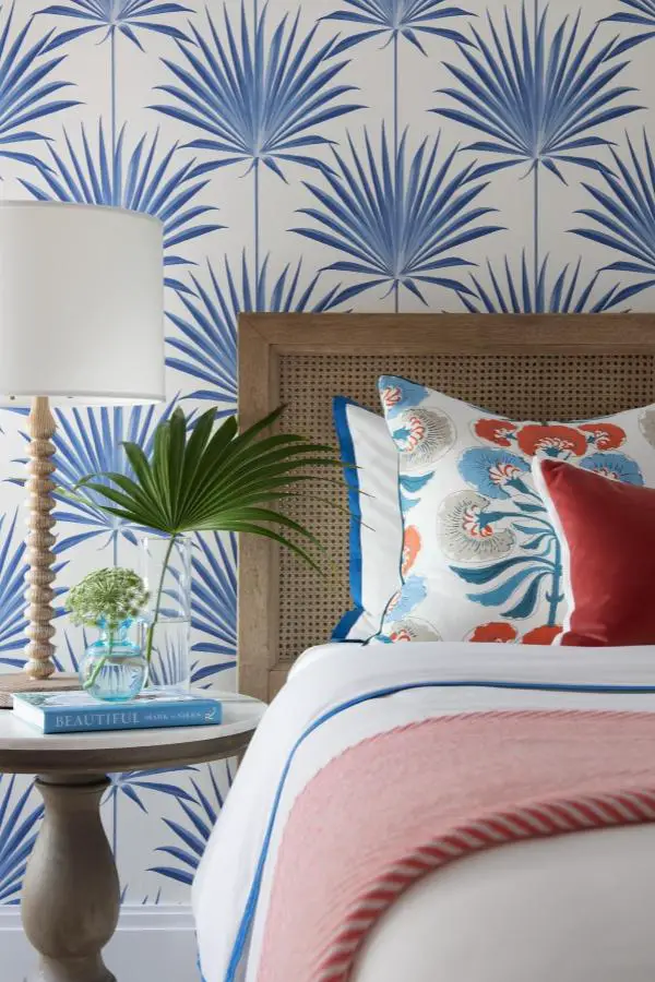 Blue palm frond wallpaper bedroom from @shani_core_interiors_. Features cane headboard and coral accent pillows.