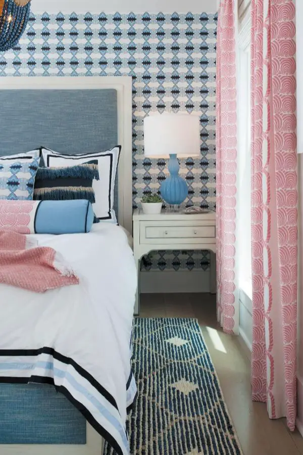 Patterned bedroom from @designershay. Blue headboard with geometric wallpaper and coral wave curtains creating layered coastal style.