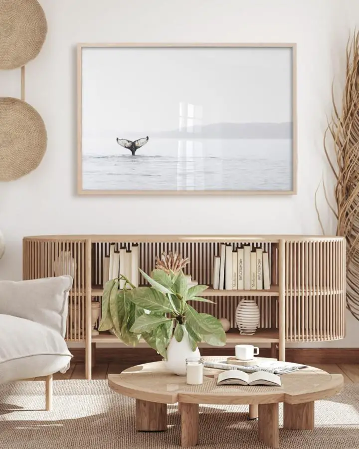 Framed whale tail photograph from @littleinkempire with natural wood credenza and coastal decor styling.