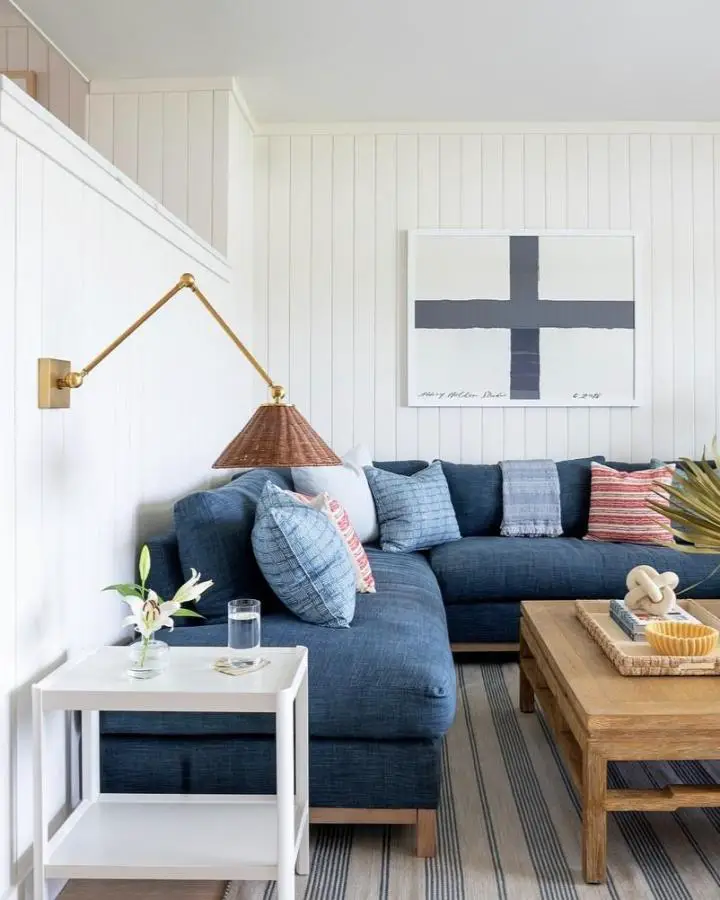 Navy sectional sofa from @lolainteriors positioned against white shiplap walls with brass swing-arm sconce and nautical artwork above.