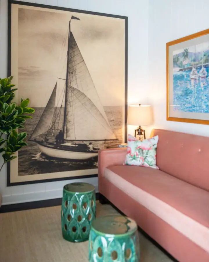 Oversized sailboat artwork from @stay.dreamspace above coral sofa with turquoise ceramic stools and nautical decor.