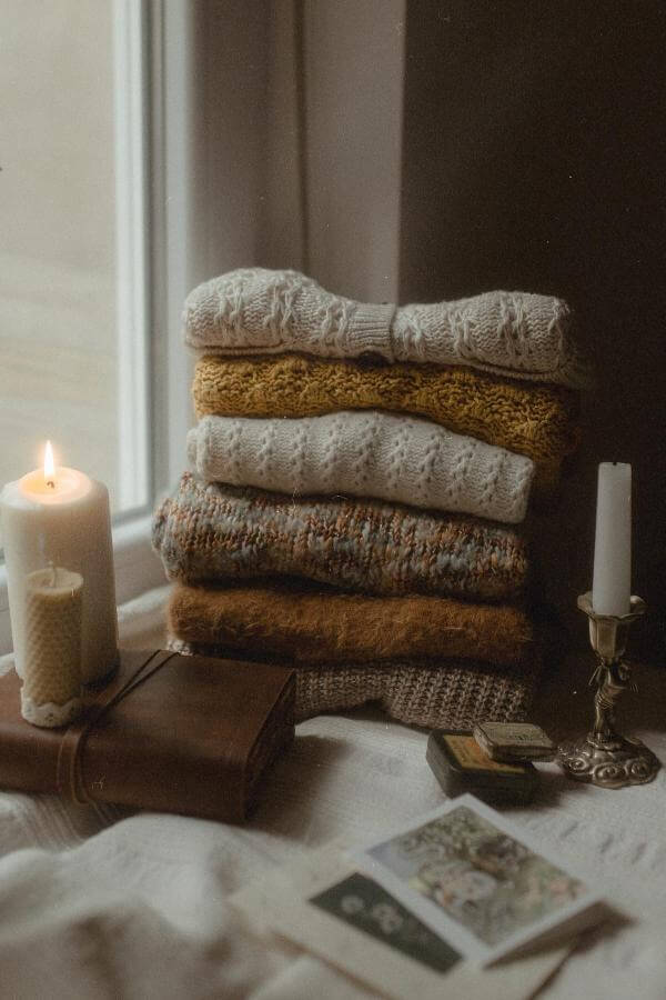 Soft cream knit blanket draped over wooden chair from @giuliaiself. Warm glow highlights cozy textures.