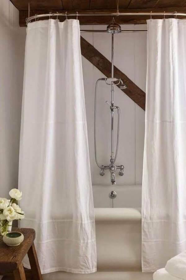 Rustic bathroom with exposed wooden beams from @ericpiasecki. White curtains frame vintage clawfoot tub underneath.
