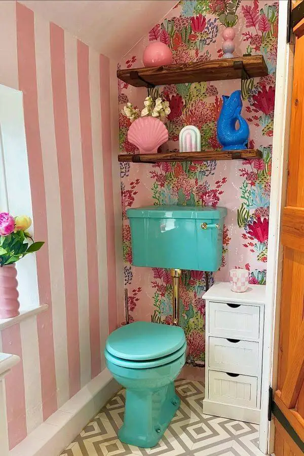 Vibrant turquoise toilet from @our_home_in_colour. Surrounded by floral wallpaper and rustic wooden shelving with decorative accessories.