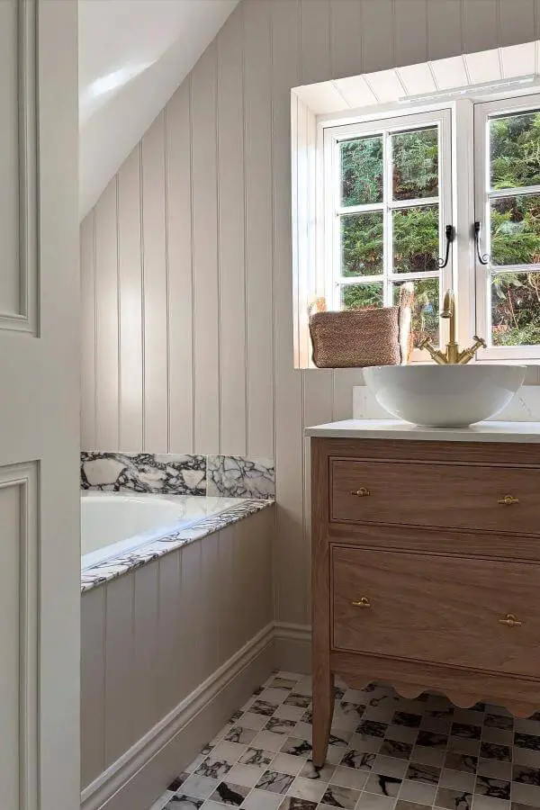 Muted gray paneled bathroom from @luce.interiordesign. Features marble tub surround and vintage-style checkered flooring.