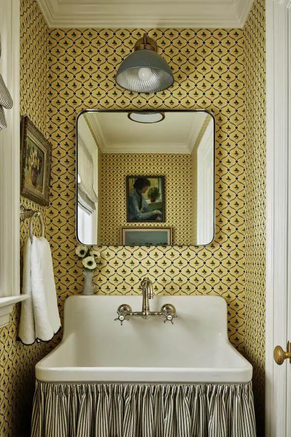 Mustard yellow geometric wallpaper powder room from @katierosenfeld. Features farmhouse sink with striped fabric skirt and vintage mirror.