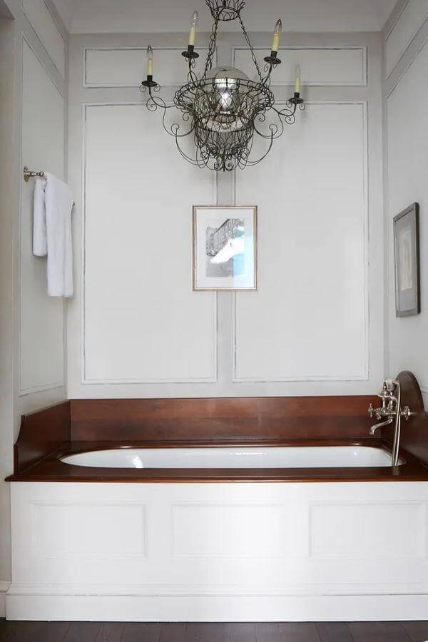 Elegant wrought iron chandelier above wooden bathtub surround from @ritakonig. Classic cottage-style bathroom design.