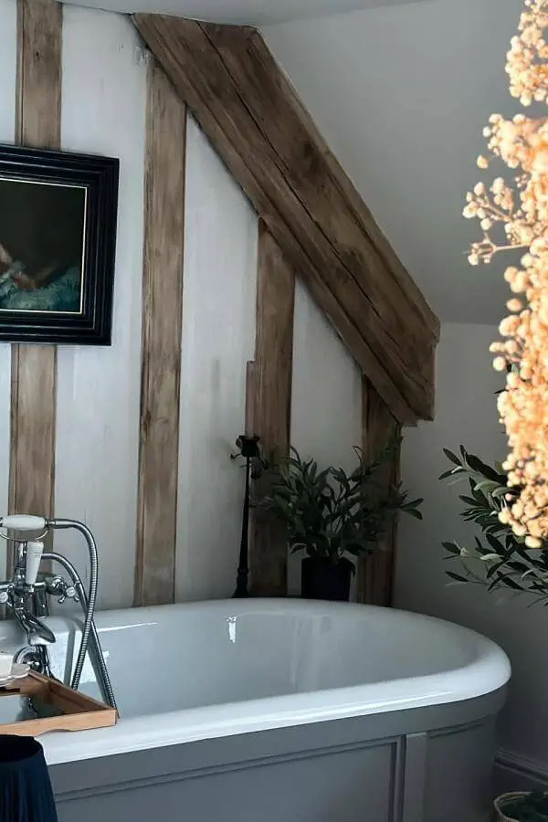 Exposed wooden beams bathroom from @thelistedtownhouse. Perfect cottagecore bathroom ideas with rustic oak framing white bathtub.