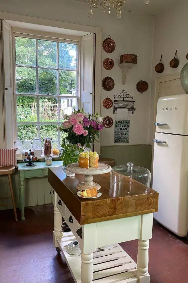 Rustic kitchen island with copper cookware collection displayed on white walls from @hillhousevintage. Green cabinets and vintage charm throughout.