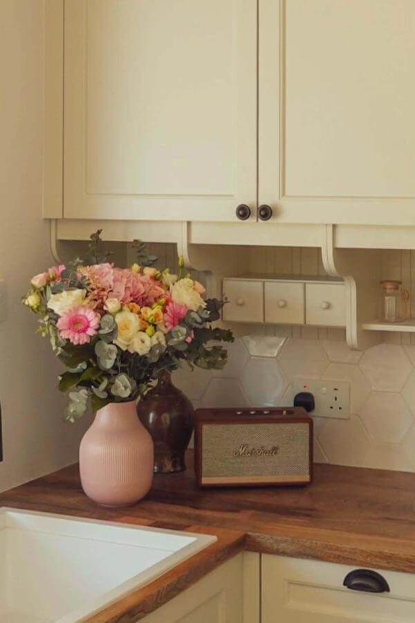 Cream vintage-style radio and pink vase with mixed flowers from @clarkesandko on wooden kitchen counter.