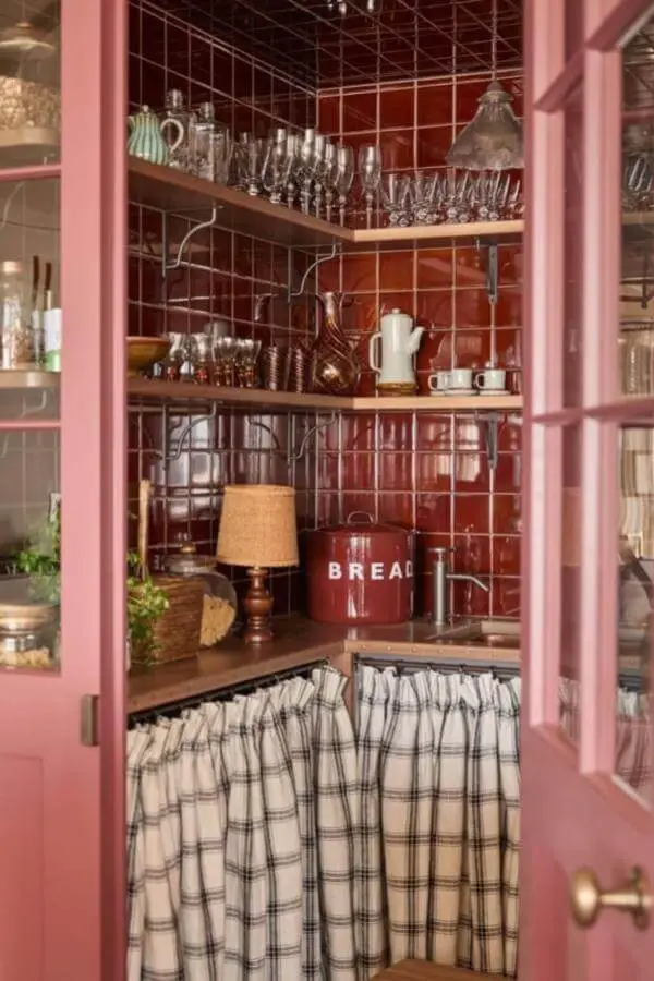 Dusty pink cabinet storage from @louiseroehome showcasing wire baskets and cottagecore kitchen ideas with checkered curtains.