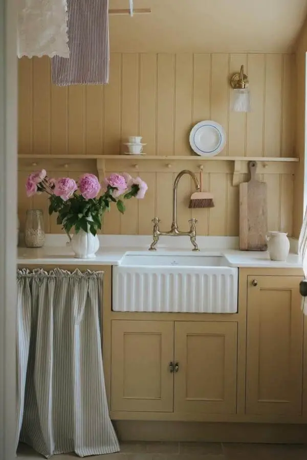 Buttery yellow kitchen with white farmhouse sink from @louiseroehome. Vintage brass faucet and striped curtain details.