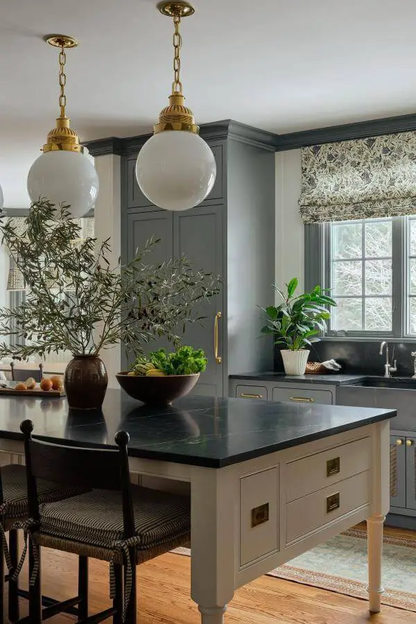 Sage green kitchen island from @katierosenfeld. Brass pendant lights and natural greenery create cozy atmosphere.