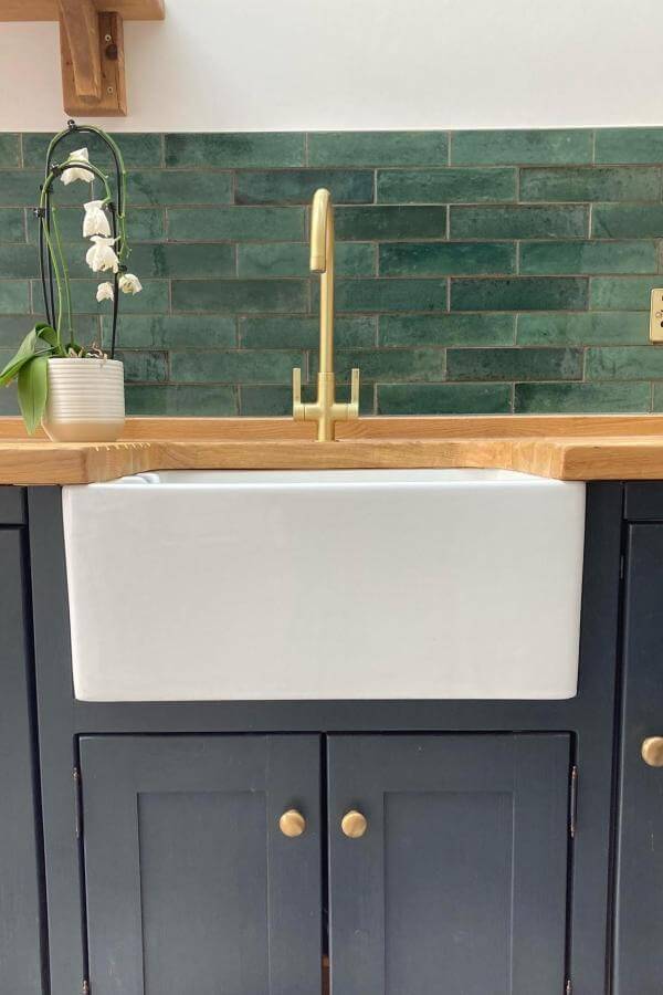Forest green subway tile backsplash with brass faucet and white farmhouse sink from @theolivebranchkitchens. Natural wood countertops complete the rustic look.