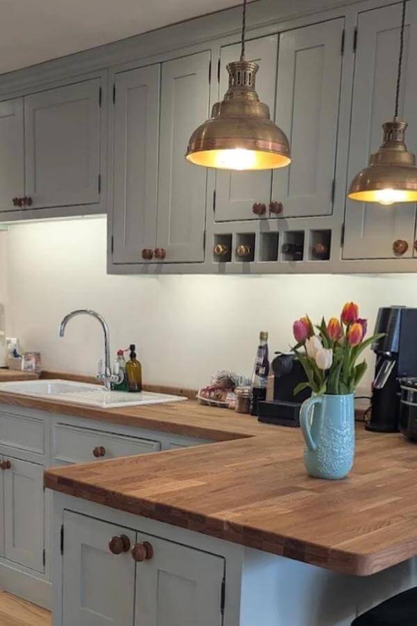 Sage green kitchen with copper pendant lights from @theolivebranchkitchens. Wood countertops and fresh tulips complete the rustic look.