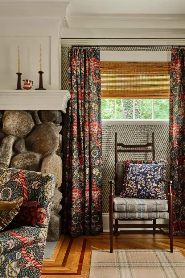 Cozy floral and plaid cushions on vintage armchair from @katierosenfeld. Mix-and-match patterns delight beside stone fireplace.